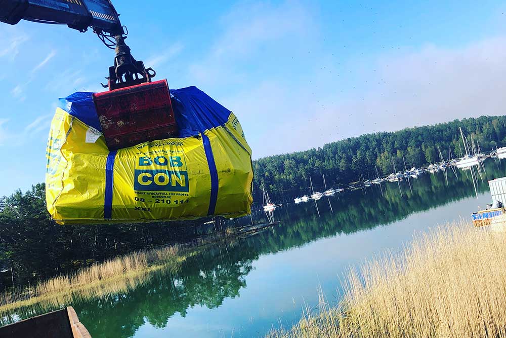Kran som lyfter BOBCONs byggsäck vid en sjö.
